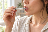 An adult blowing gently through the flared mouthpiece of the AUM Resonance sound pendant.