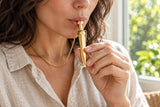 An adult using the gold-tone pendant for a gentle exhale beside a bright window.
