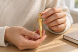 Hands holding the gold-tone geometric pendant during a quiet pause at a desk.