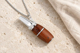 Walnut Woodland Pause pendant with a polished metal mouthpiece on pale stone.